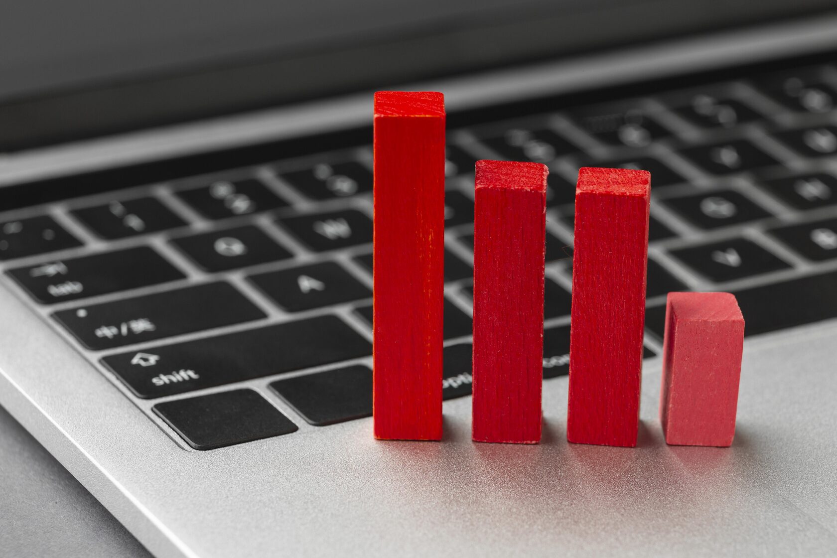 Red wooden bar chart blocks placed on a laptop keyboard, symbolizing financial data, declining metrics, or digital payment performance trends.